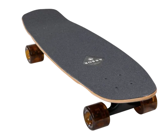 A longboard skateboard with a dark gray grip tape deck, natural wood edge, and translucent amber-brown wheels, shown on a light gray background with navigation arrows.